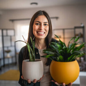 Portrait of beautiful woman stand and hold flower pots at home