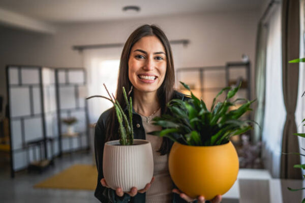Portrait of beautiful woman stand and hold flower pots at home